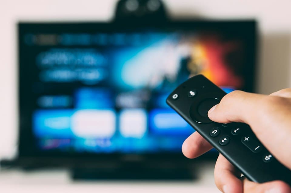Hand mit Fernbedienung vor einem Fernseher mit unscharfer App-Oberfläche