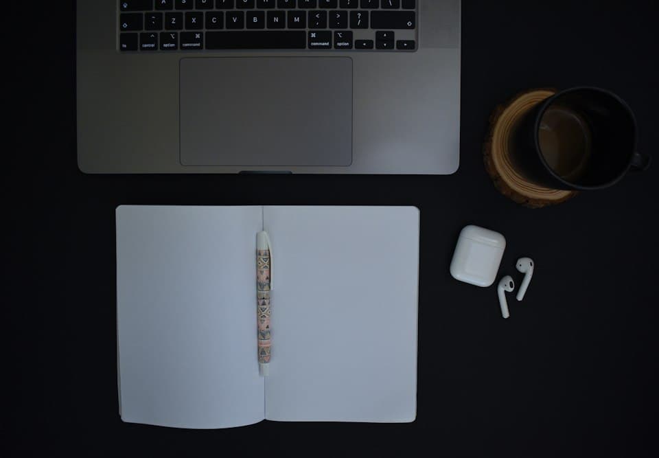 Laptop, Notizbuch und Kaffeetasse auf einem dunklen Schreibtisch
