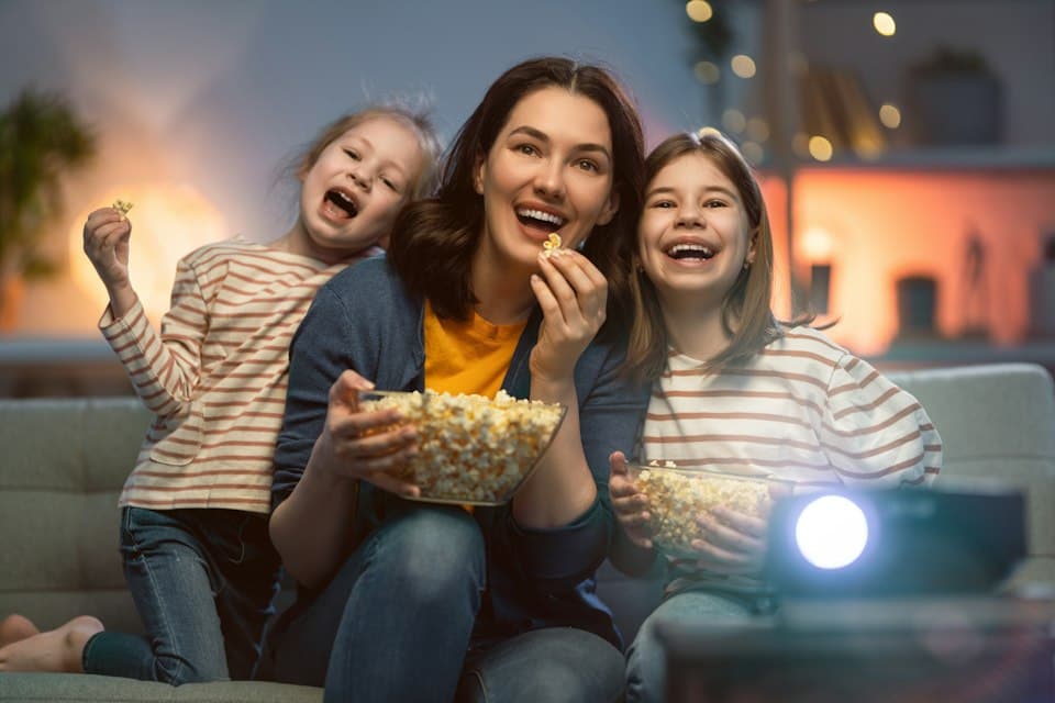 Frau und zwei Kinder mit Popcorn beim Filmabend mit Projektor