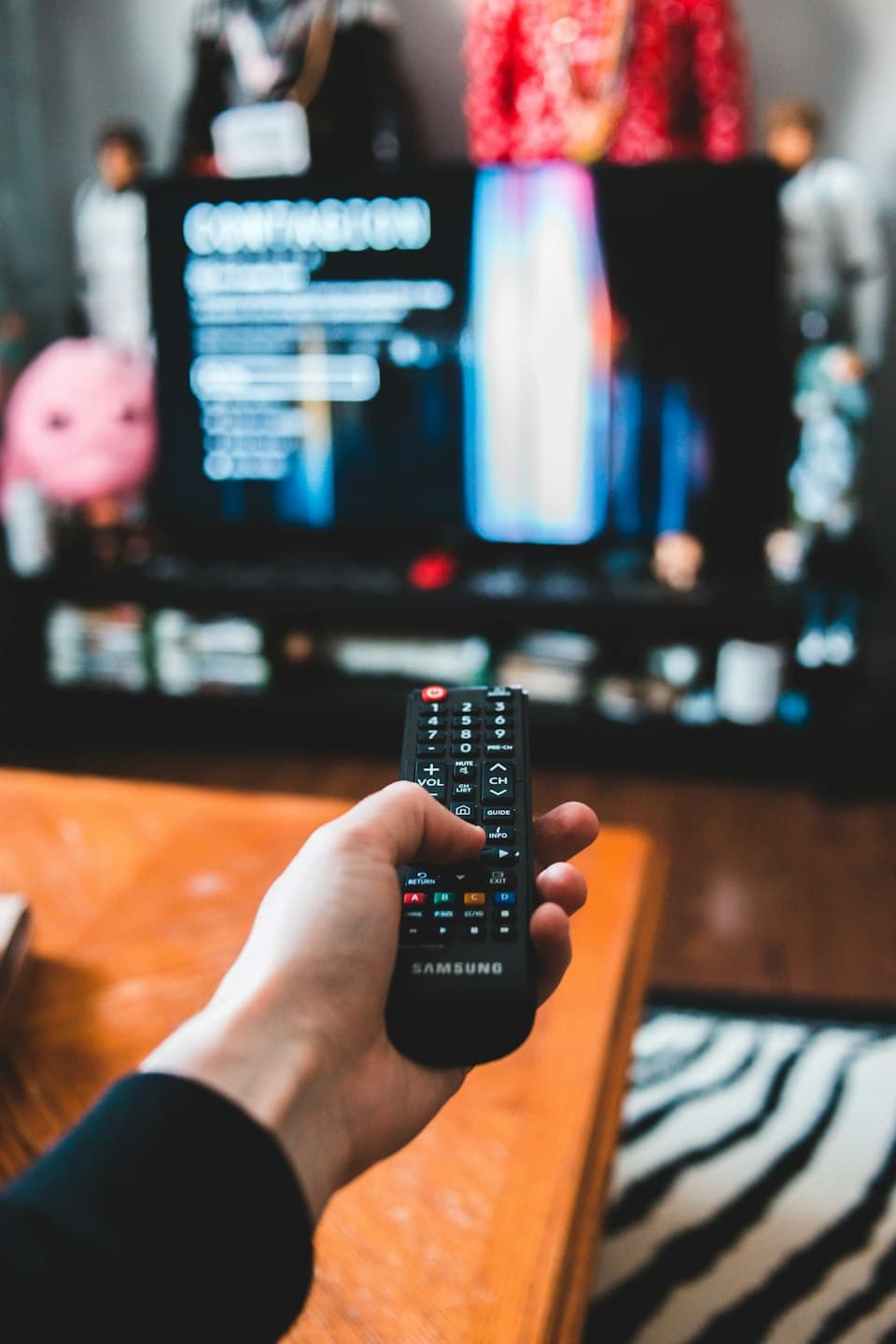 Hand mit Fernbedienung vor einem unscharfen Fernseher
