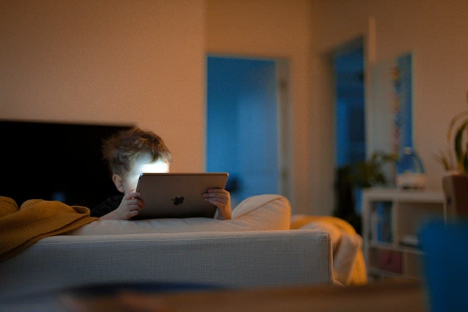 Kind auf dem Sofa schaut auf ein Tablet