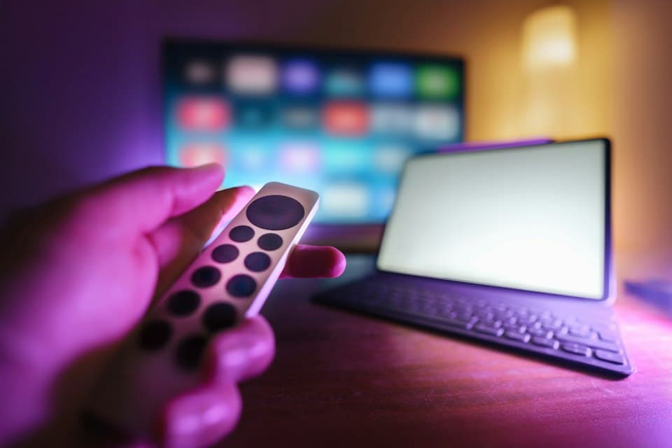 Hand mit Fernbedienung vor einem Fernseher in violettem Licht