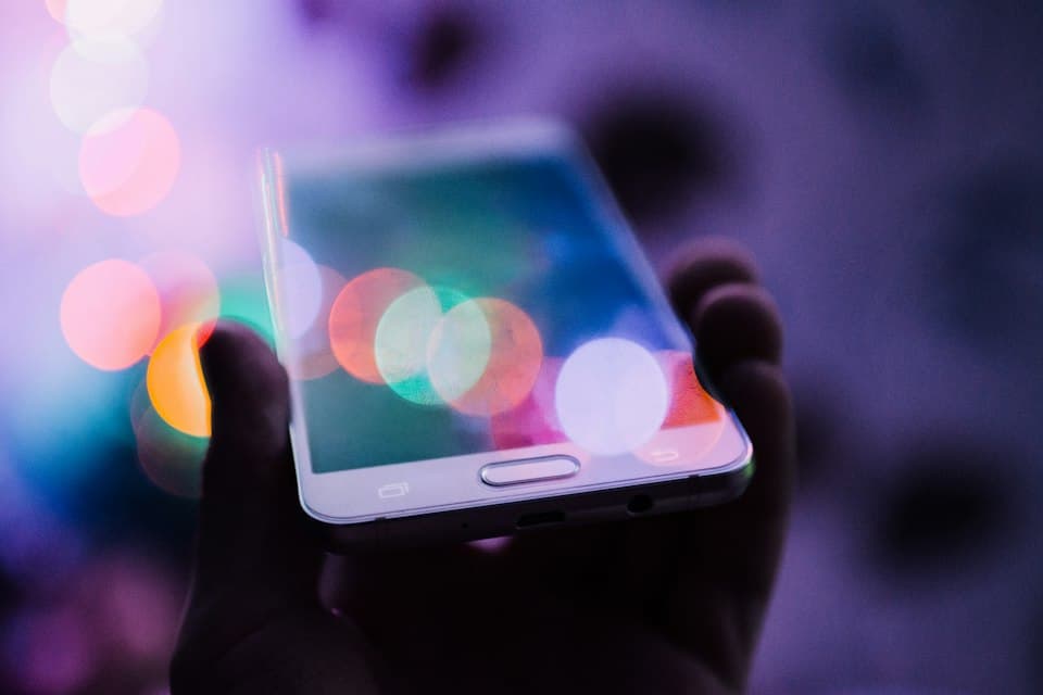 Hand hält ein Smartphone vor violettem, unscharfem Hintergrund