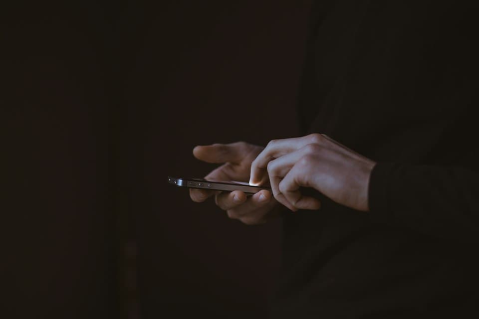 Hände mit Smartphone in einem dunklen Raum